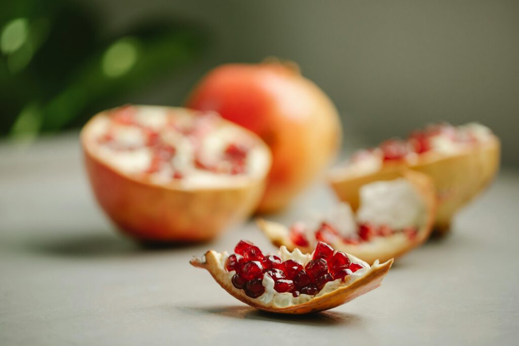 Several pomegranates are on a table. The picture focuses on a piece of the fruit that shows the red seeds.