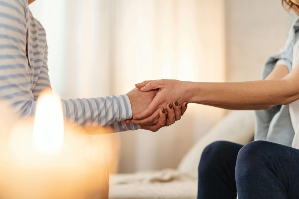 Two people sit across from each other, holding hands. A candle is in the foreground.